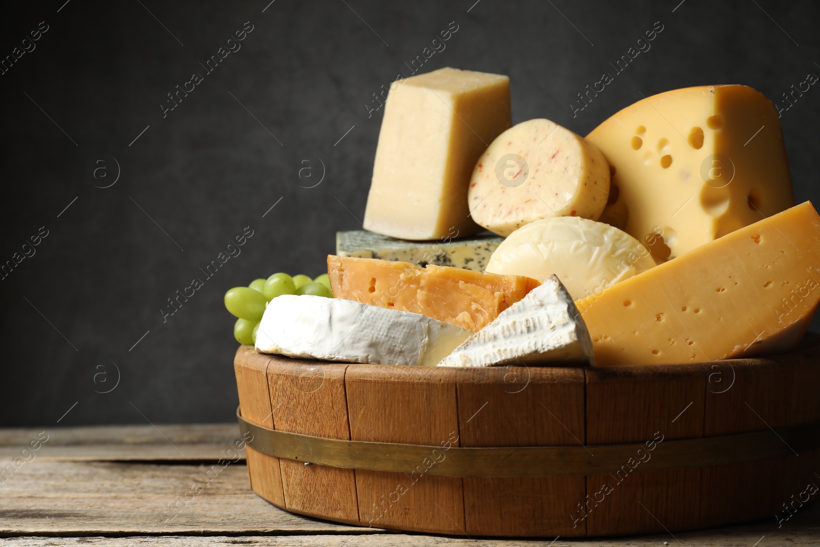 Photo of Different types of cheese and grapes on wooden table, closeup. Space for text