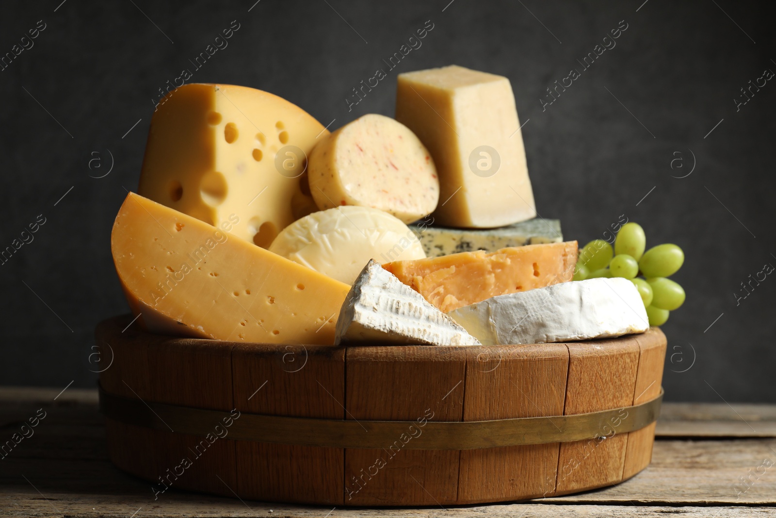 Photo of Different types of cheese and grapes on wooden table, closeup