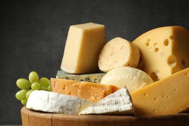 Photo of Different types of cheese and grapes in wooden tray on grey background, closeup