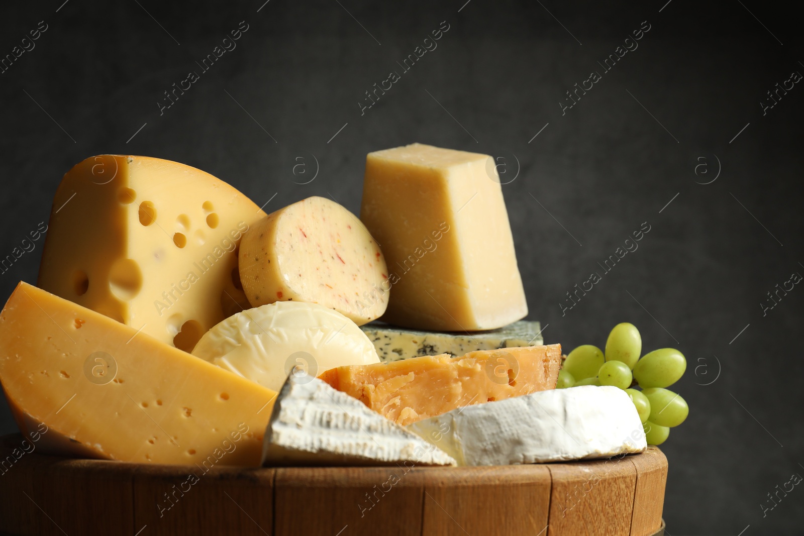 Photo of Different types of cheese and grapes in wooden tray on grey background, closeup