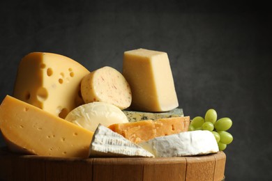 Photo of Different types of cheese and grapes in wooden tray on grey background, closeup