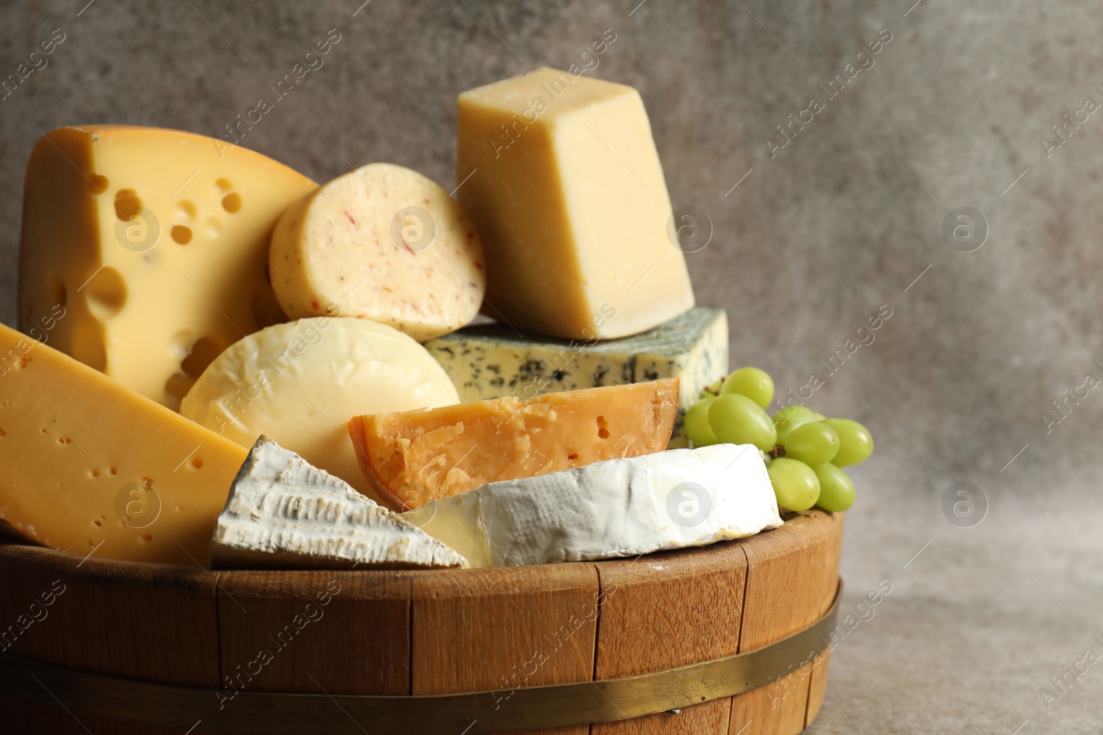 Photo of Different types of cheese and grapes in tray on grey table, closeup. Space for text