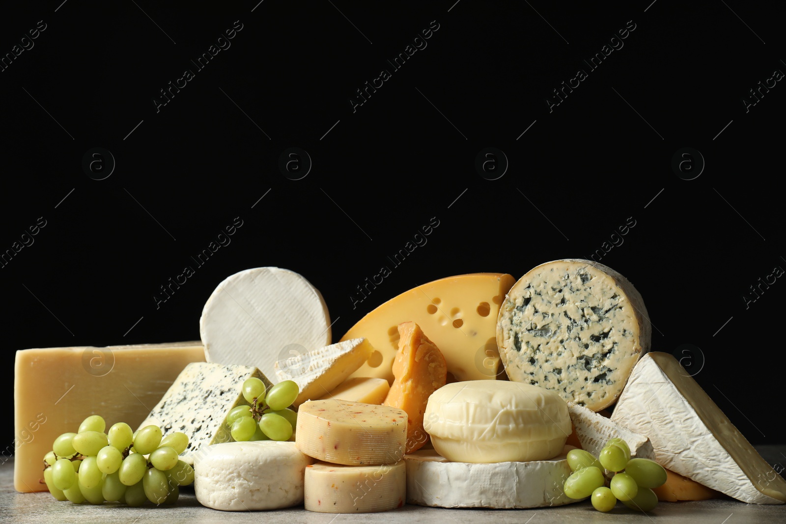 Photo of Different types of cheese and grapes on grey table against black background