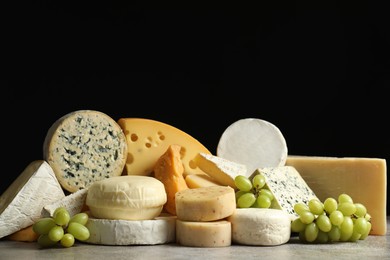 Photo of Different types of cheese and grapes on grey table against black background