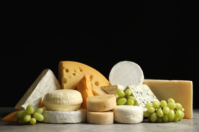 Photo of Different types of cheese and grapes on grey table against black background