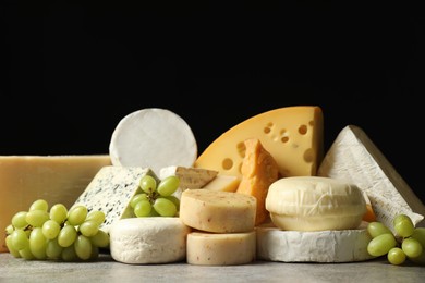 Photo of Different types of cheese and grapes on grey table against black background