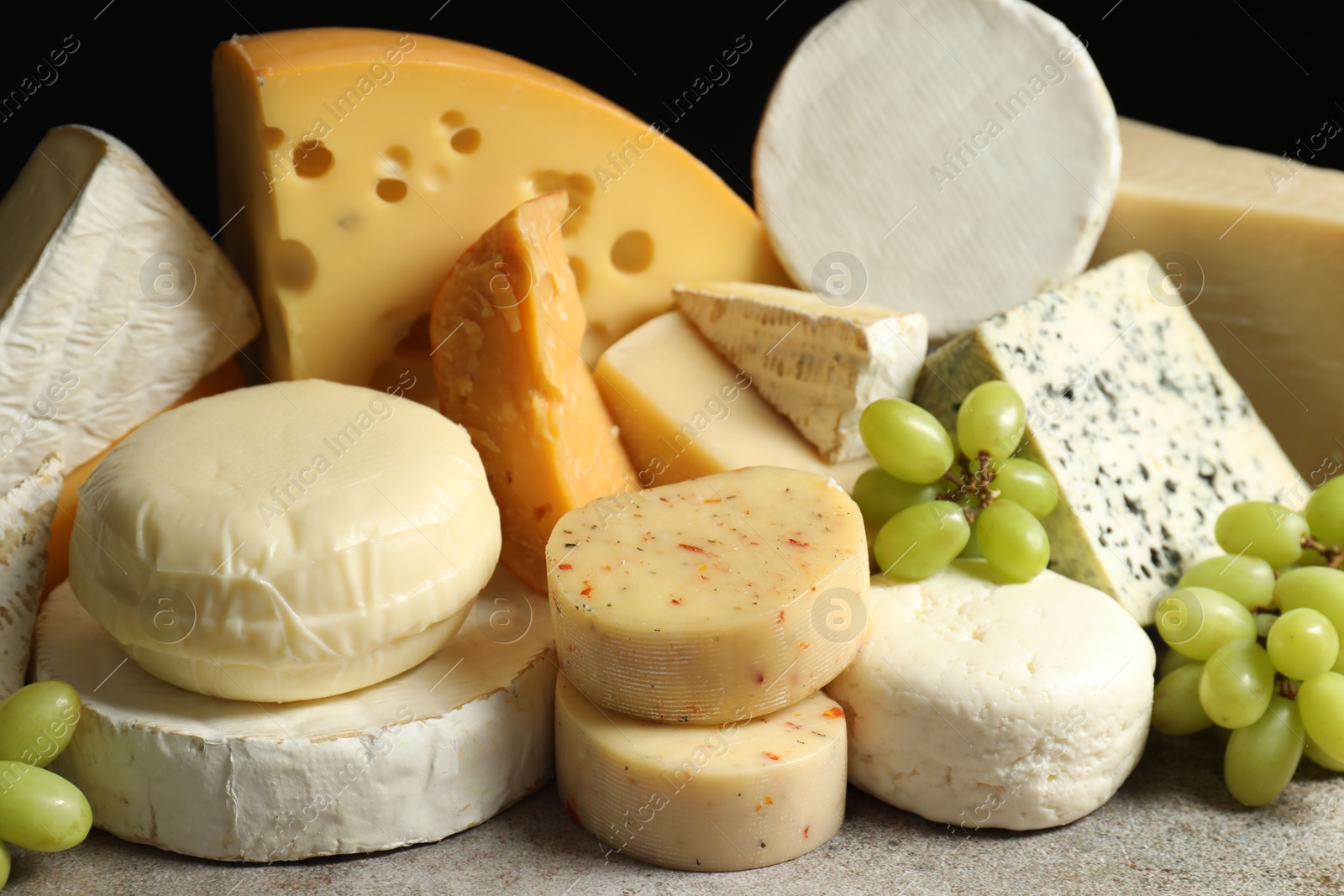 Photo of Different types of cheese and grapes on grey table, closeup