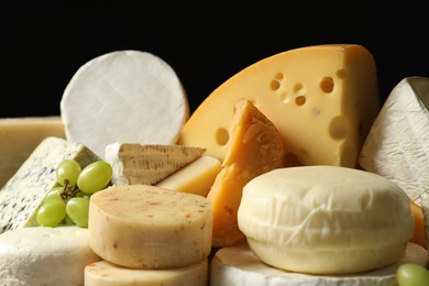 Photo of Different types of cheese and grapes on black background, closeup