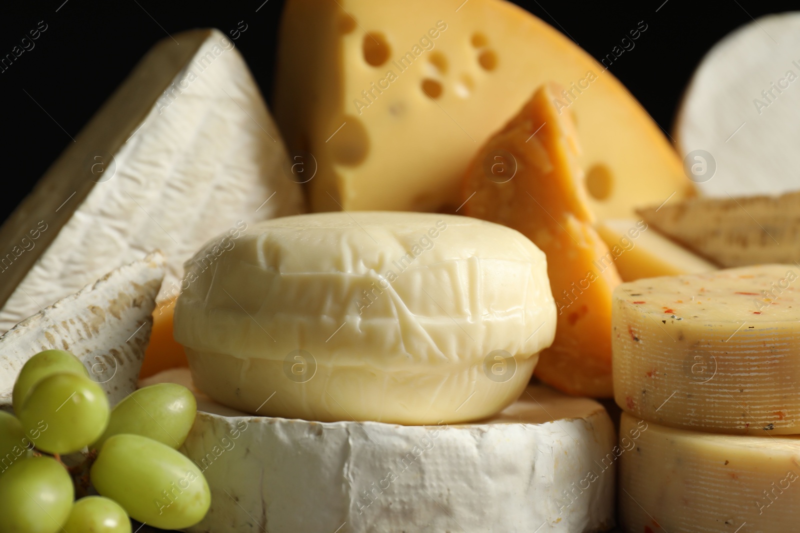 Photo of Different types of cheese and grapes on black background, closeup