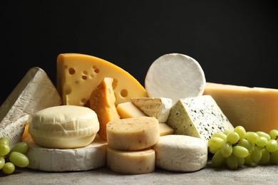 Photo of Different types of cheese and grapes on grey table against black background