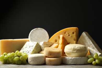 Photo of Different types of cheese and grapes on grey table against black background