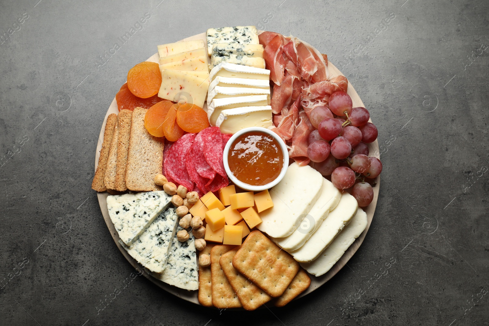 Photo of Different types of cut cheese and other snacks on grey textured table, top view