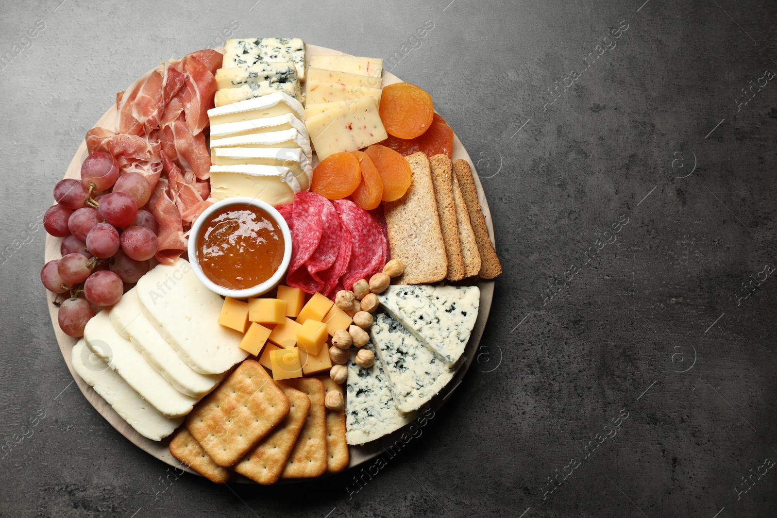 Photo of Different types of cut cheese and other snacks on grey textured table, top view. Space for text