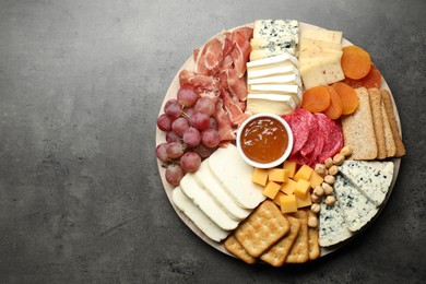 Photo of Different types of cut cheese and other snacks on grey textured table, top view. Space for text