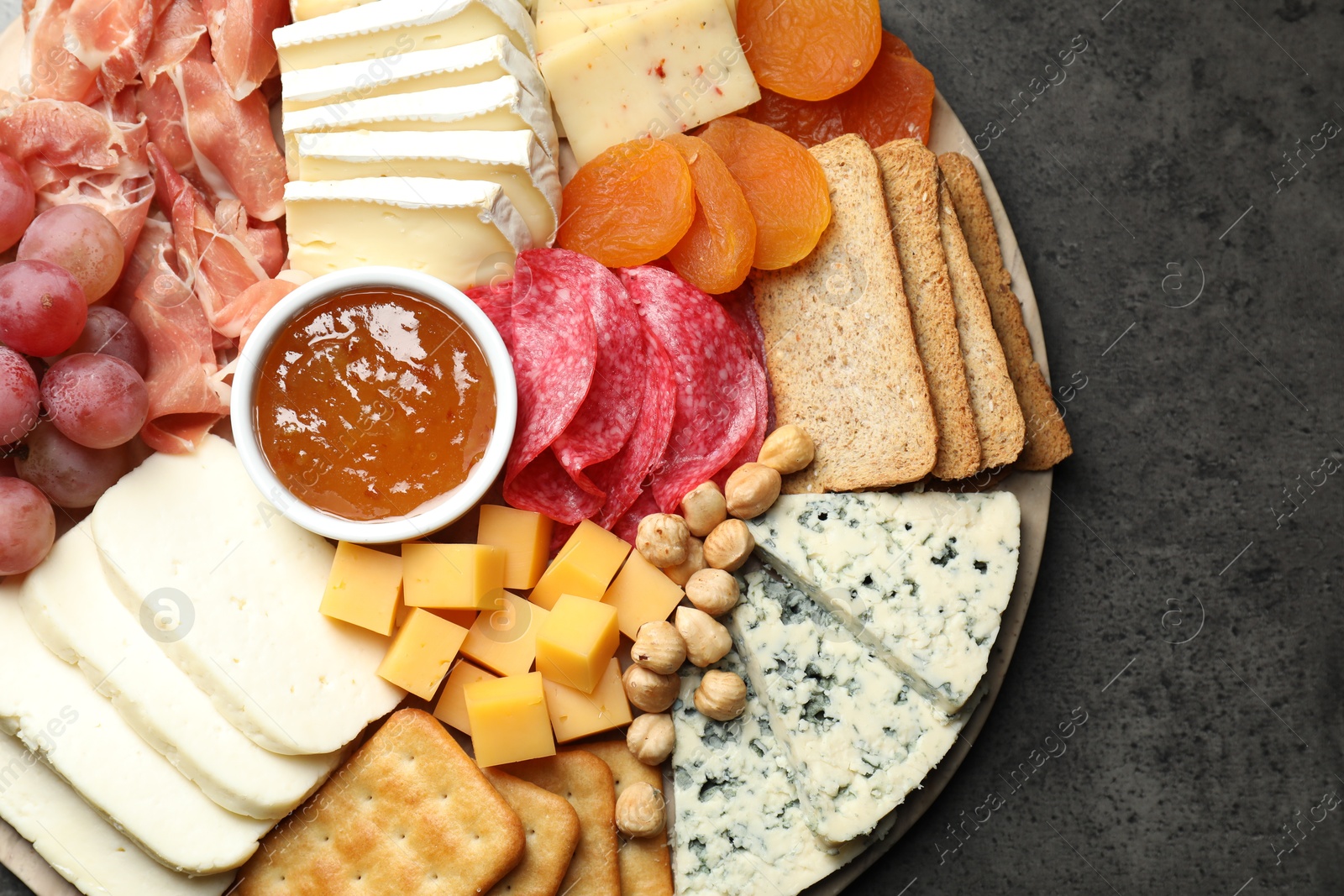 Photo of Different types of cut cheese and other snacks on grey textured table, top view