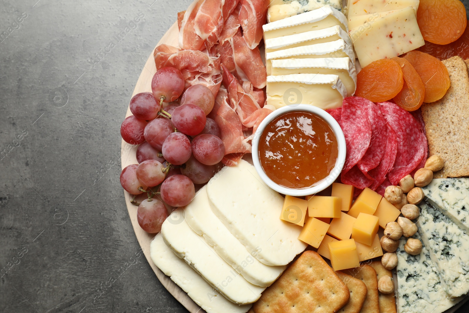 Photo of Different types of cut cheese and other snacks on grey textured table, top view. Space for text