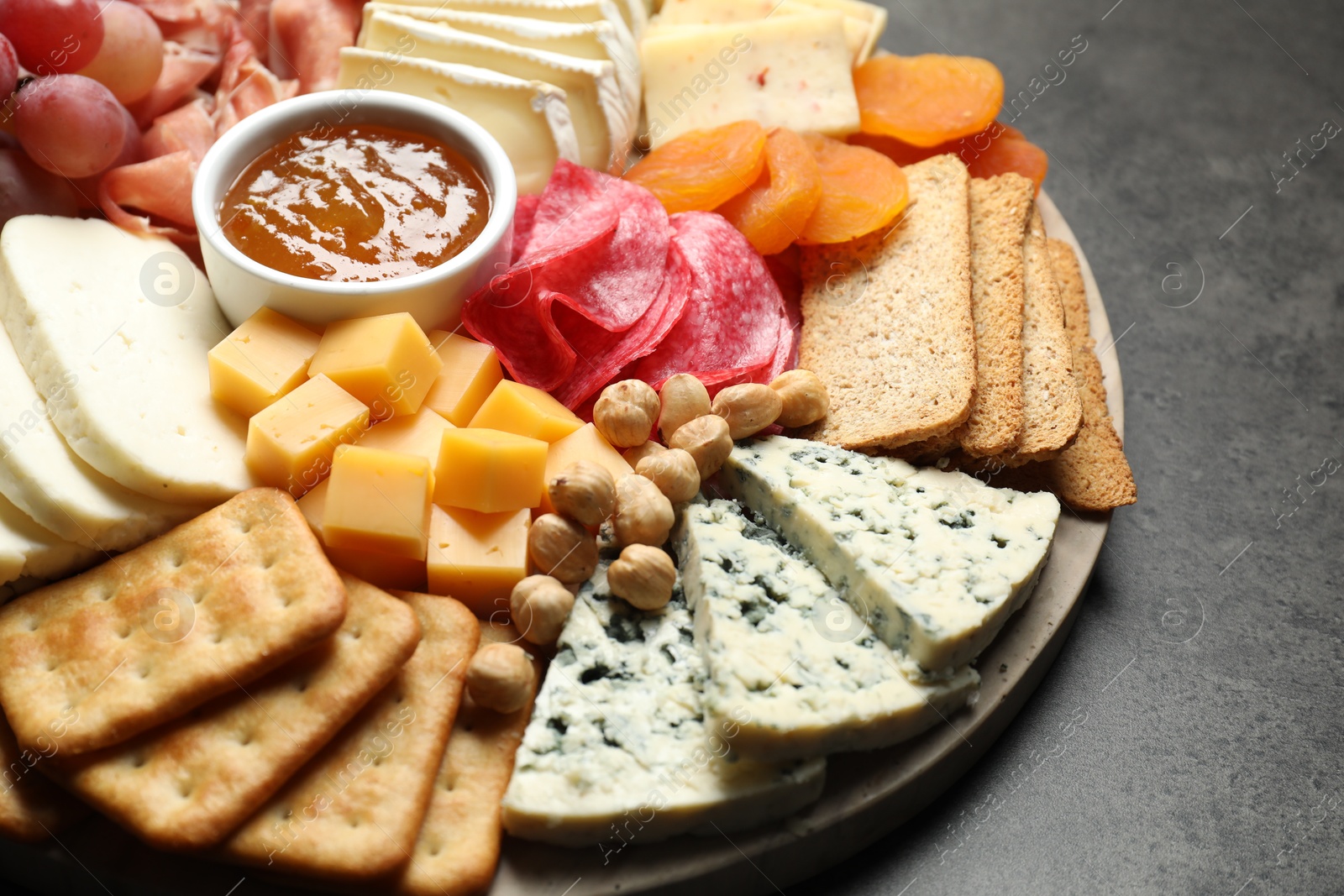 Photo of Different types of cut cheese and other snacks on grey textured table, closeup