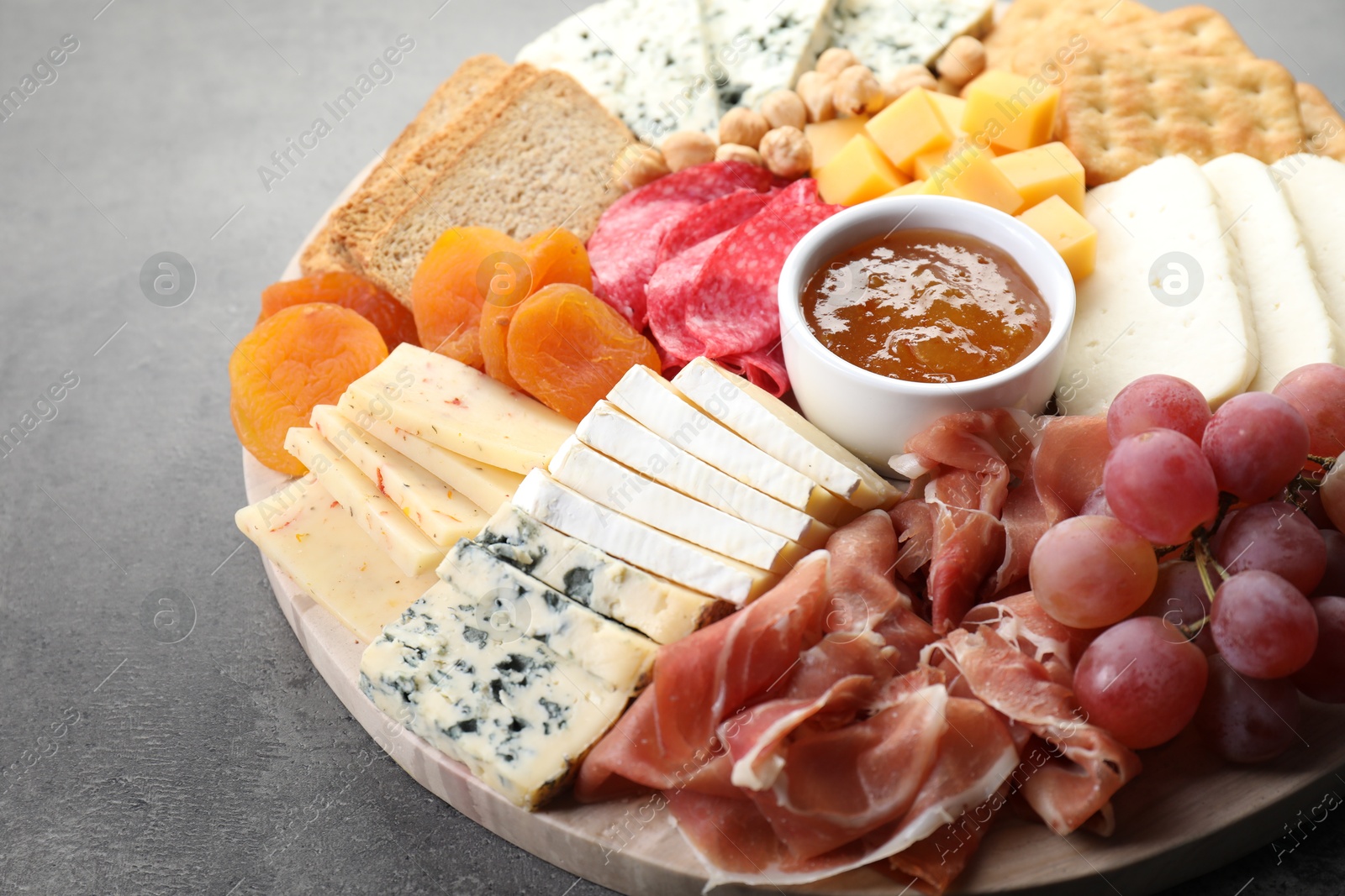 Photo of Different types of cut cheese and other snacks on grey textured table, closeup