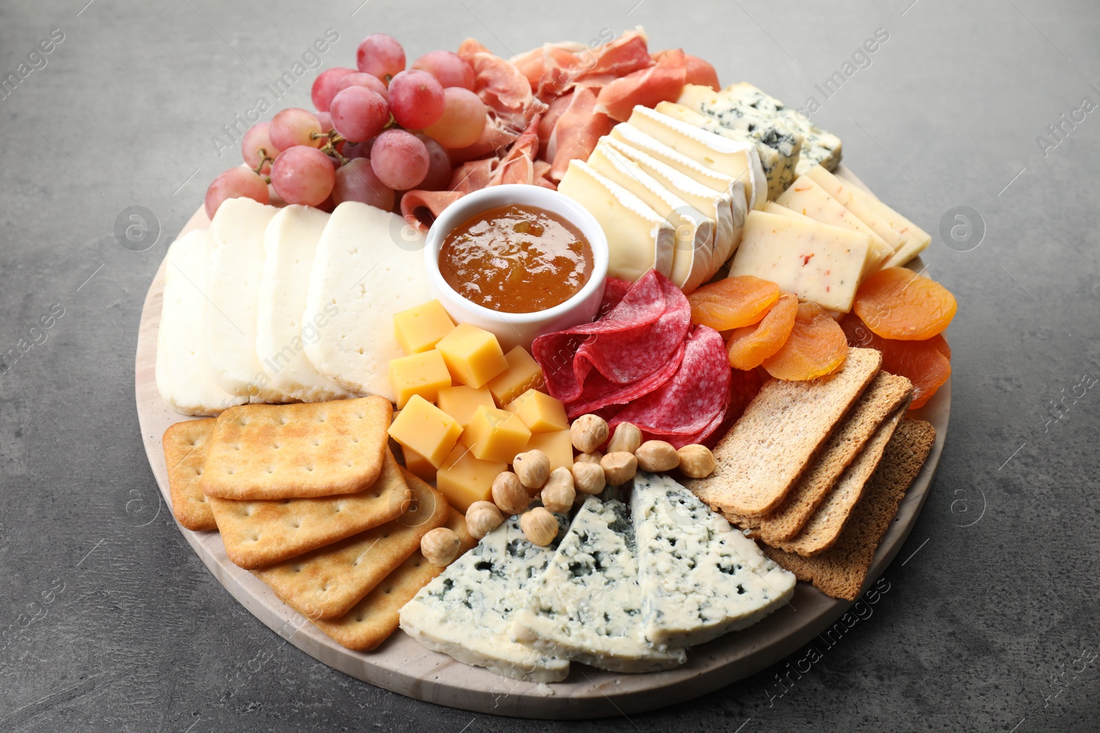 Photo of Different types of cut cheese and other snacks on grey textured table, closeup