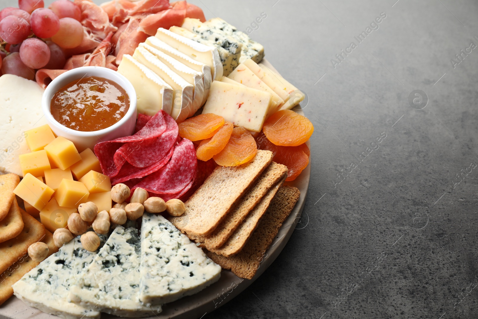 Photo of Different types of cut cheese and other snacks on grey textured table, closeup. Space for text