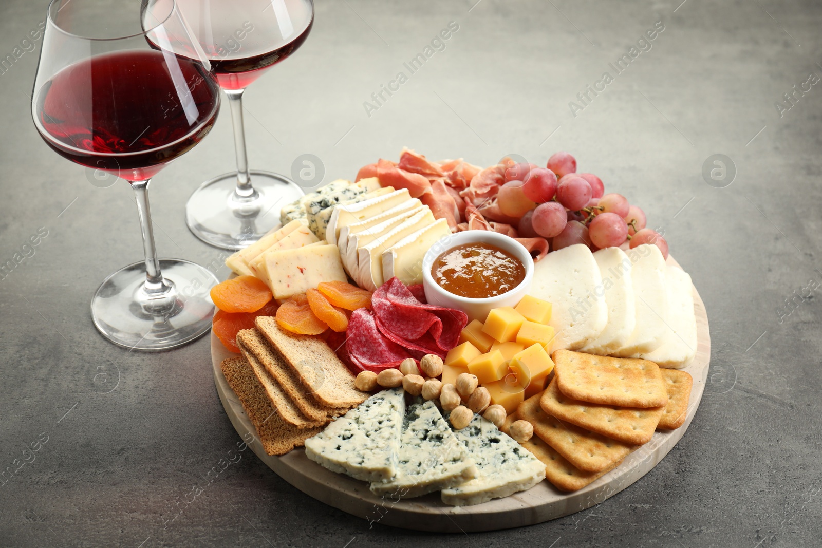 Photo of Different types of cut cheese and other snacks served with wine on grey textured table, closeup