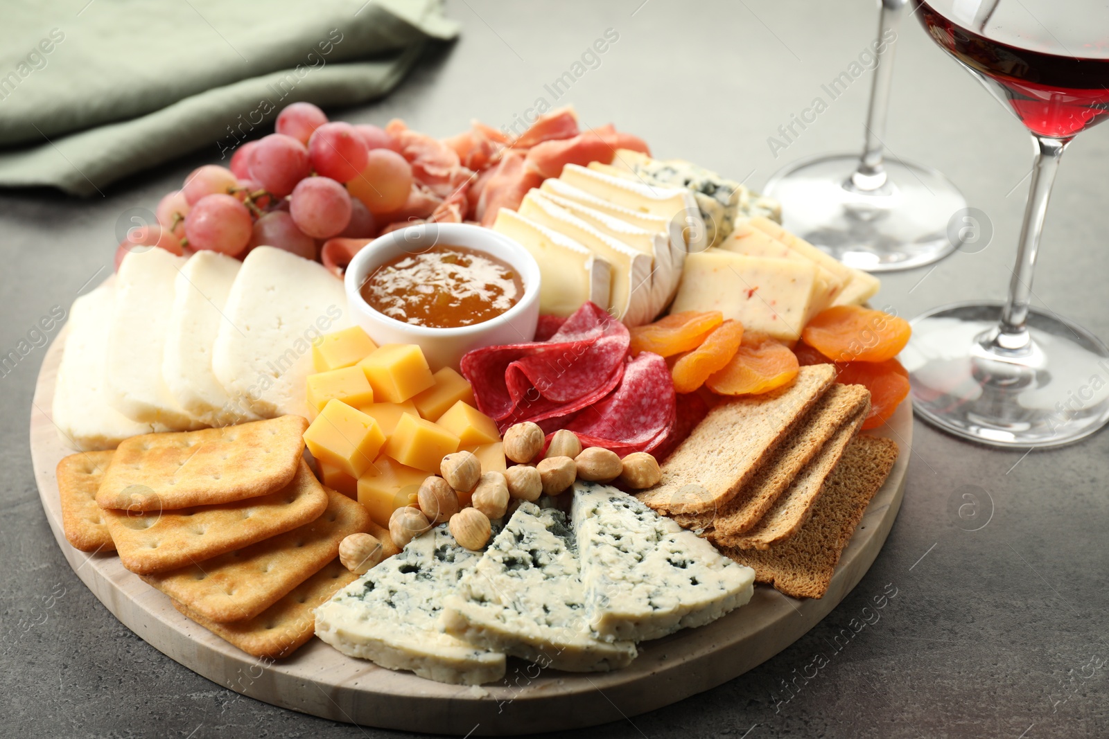 Photo of Different types of cut cheese and other snacks on grey textured table, closeup