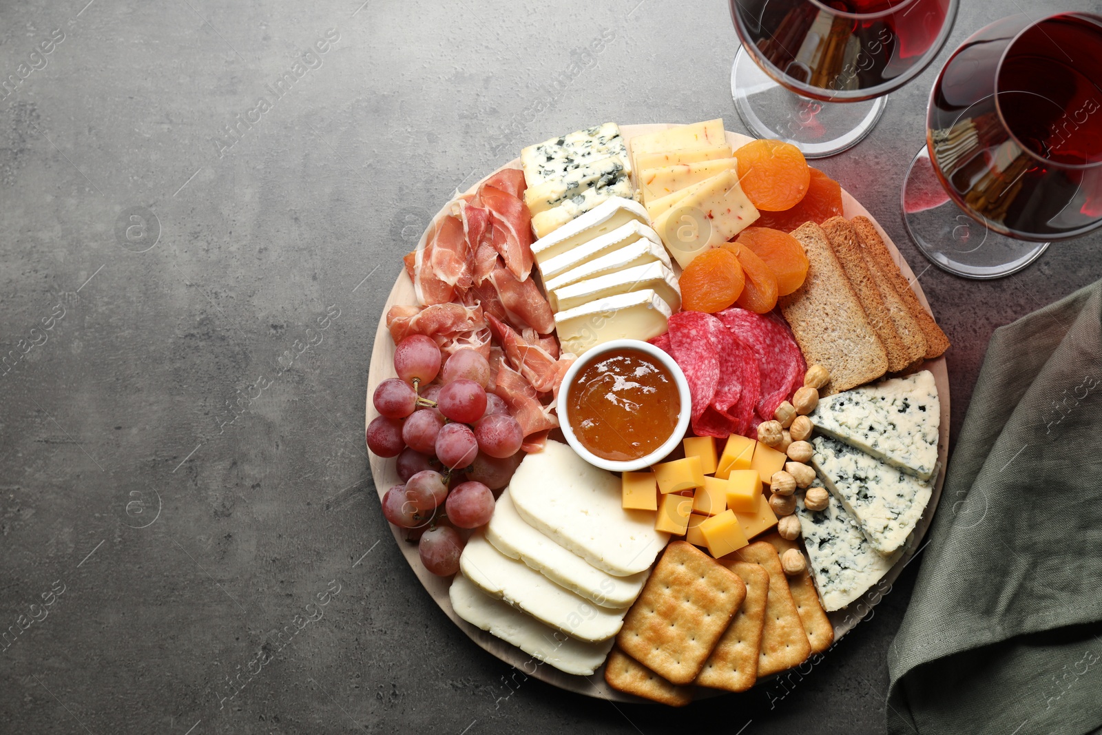 Photo of Different types of cut cheese and other snacks served with wine on grey textured table, flat lay. Space for text