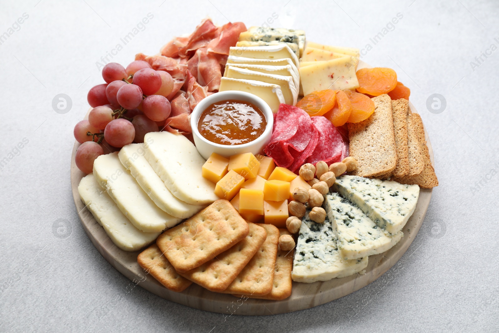 Photo of Different types of cut cheese and other snacks on light textured table, closeup