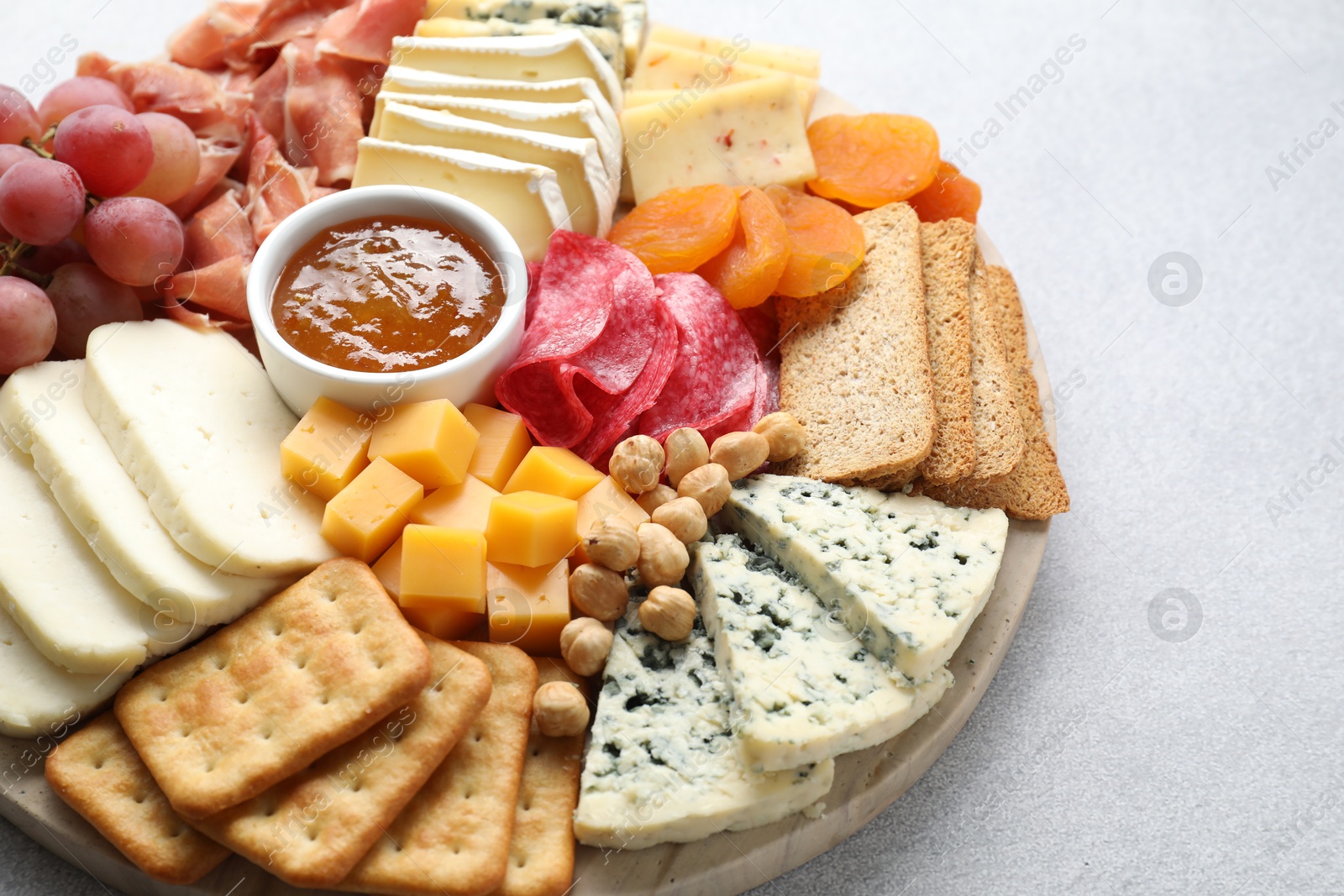 Photo of Different types of cut cheese and other snacks on light textured table, closeup