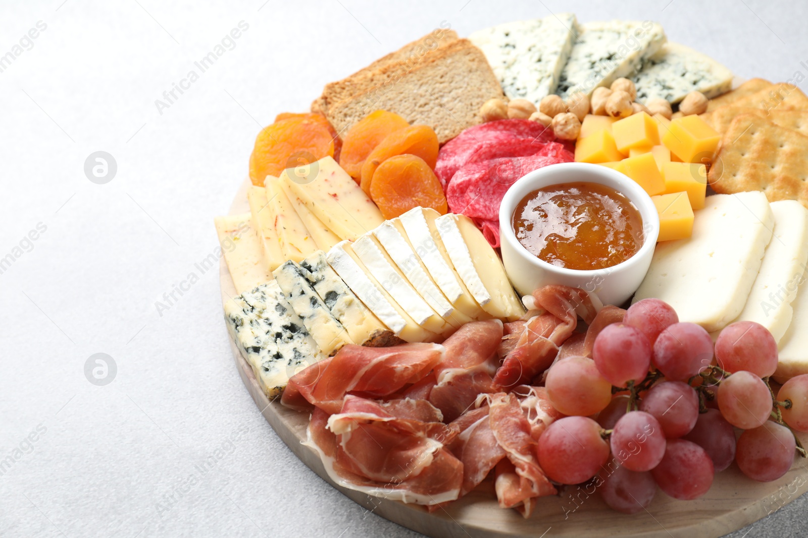 Photo of Different types of cut cheese and other snacks on light textured table, closeup