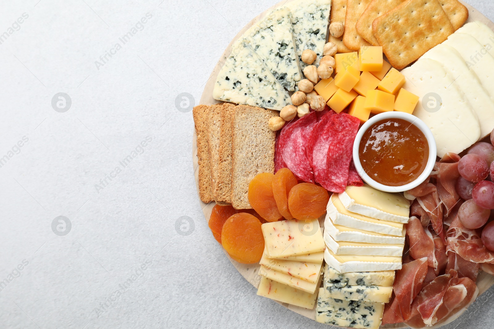 Photo of Different types of cut cheese and other snacks on light textured table, top view. Space for text