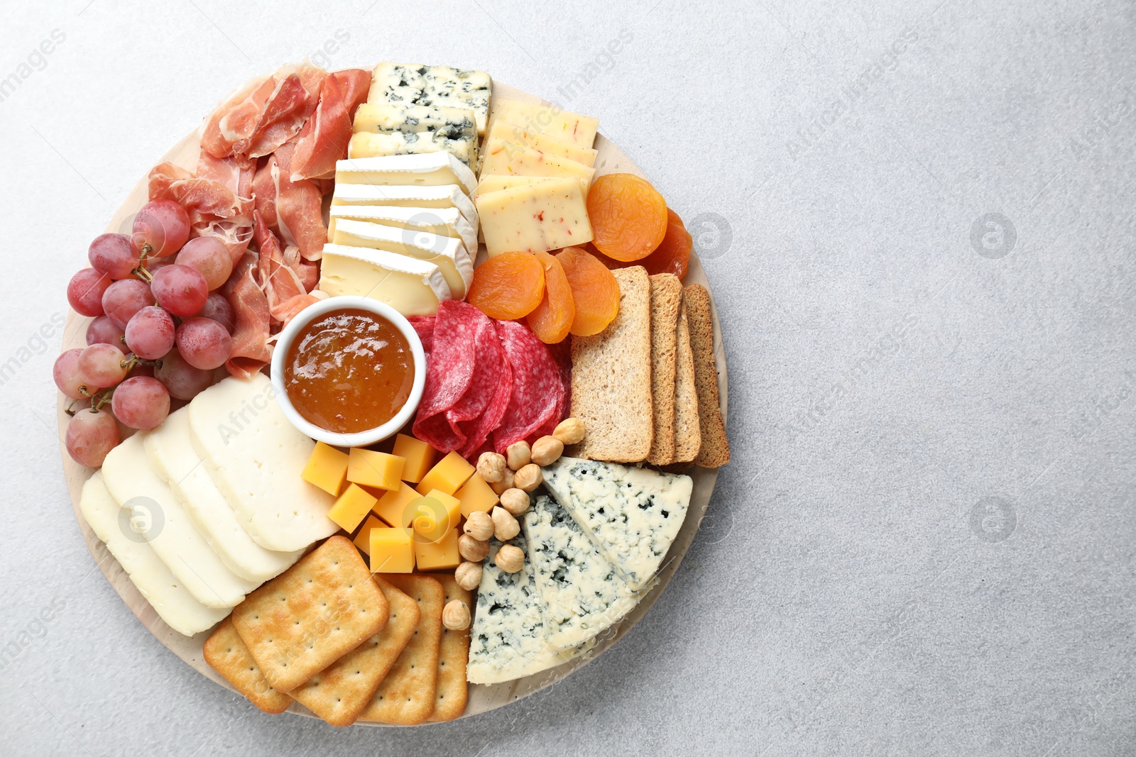 Photo of Different types of cut cheese and other snacks on light textured table, top view. Space for text