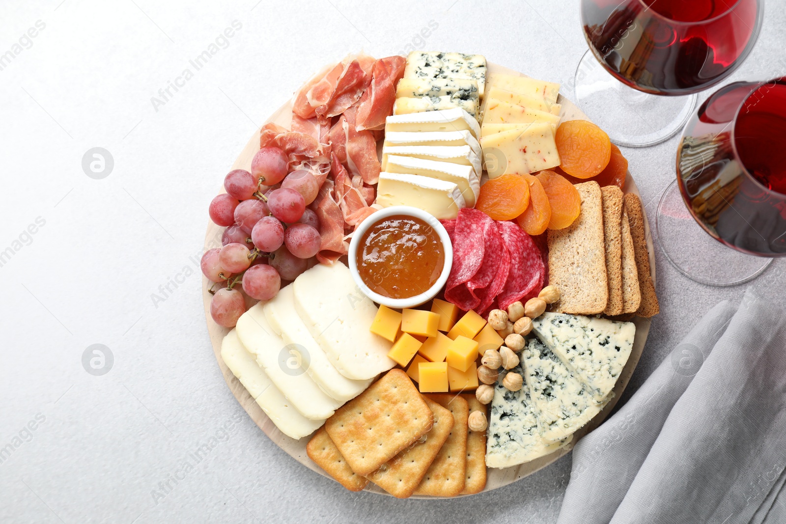 Photo of Different types of cut cheese and other snacks served with wine on light textured table, flat lay. Space for text