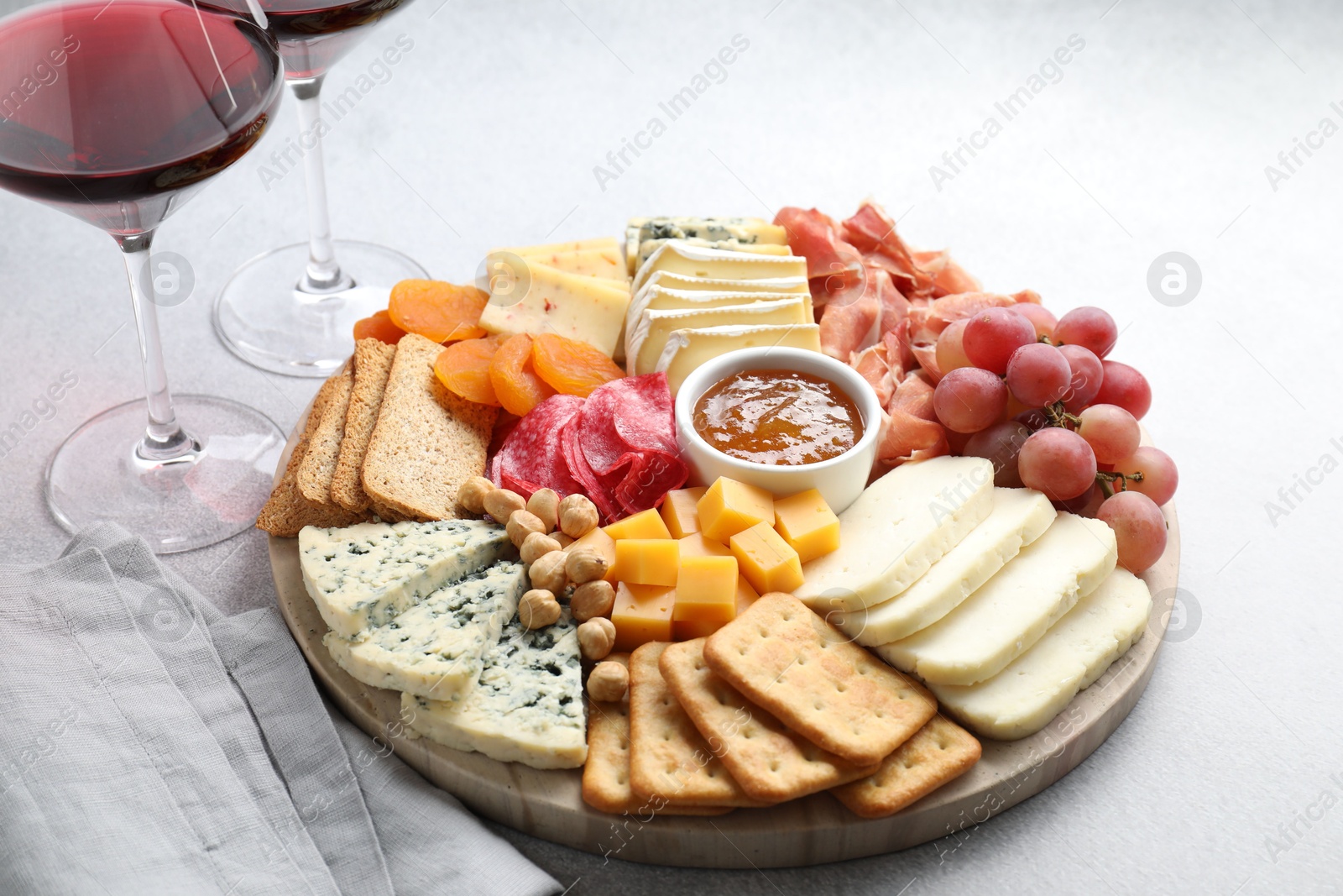 Photo of Different types of cut cheese and other snacks served with wine on light textured table, closeup