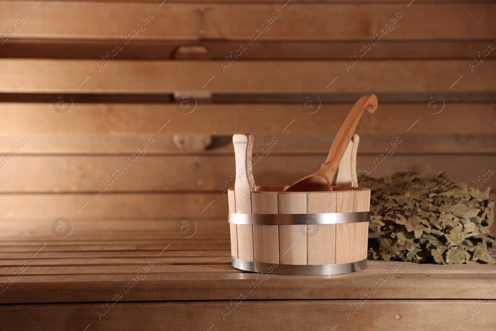 Photo of Bucket, ladle and whisk on wooden bench in sauna. Space for text