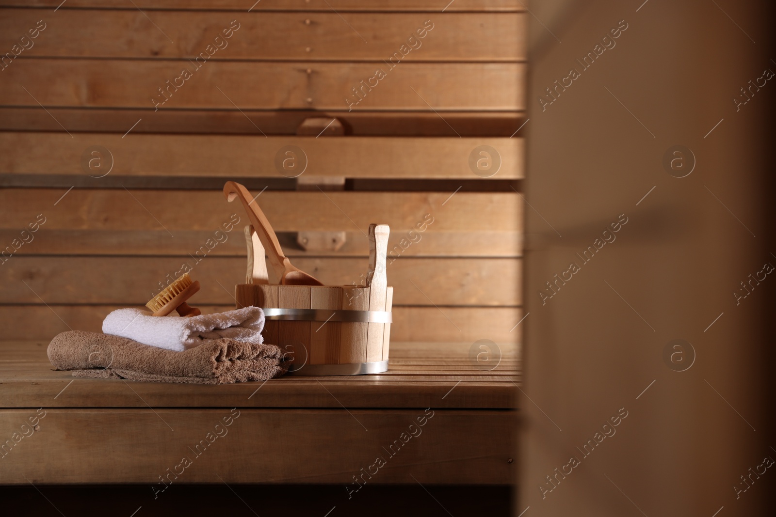 Photo of Bucket, ladle, massaging brush and stack of towels on wooden bench in sauna. Space for text