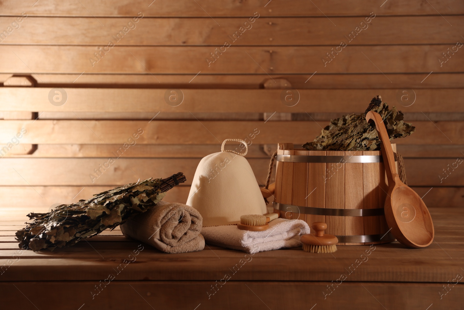 Photo of Bucket, whisks, massaging brushes and other equipment on wooden bench in sauna