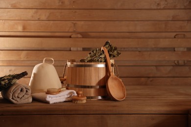 Photo of Bucket, whisk, massaging brushes and other equipment on wooden bench in sauna. Space for text