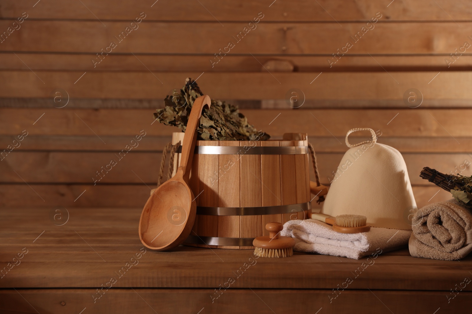 Photo of Bucket, whisk, massaging brushes and other equipment on wooden bench in sauna. Space for text