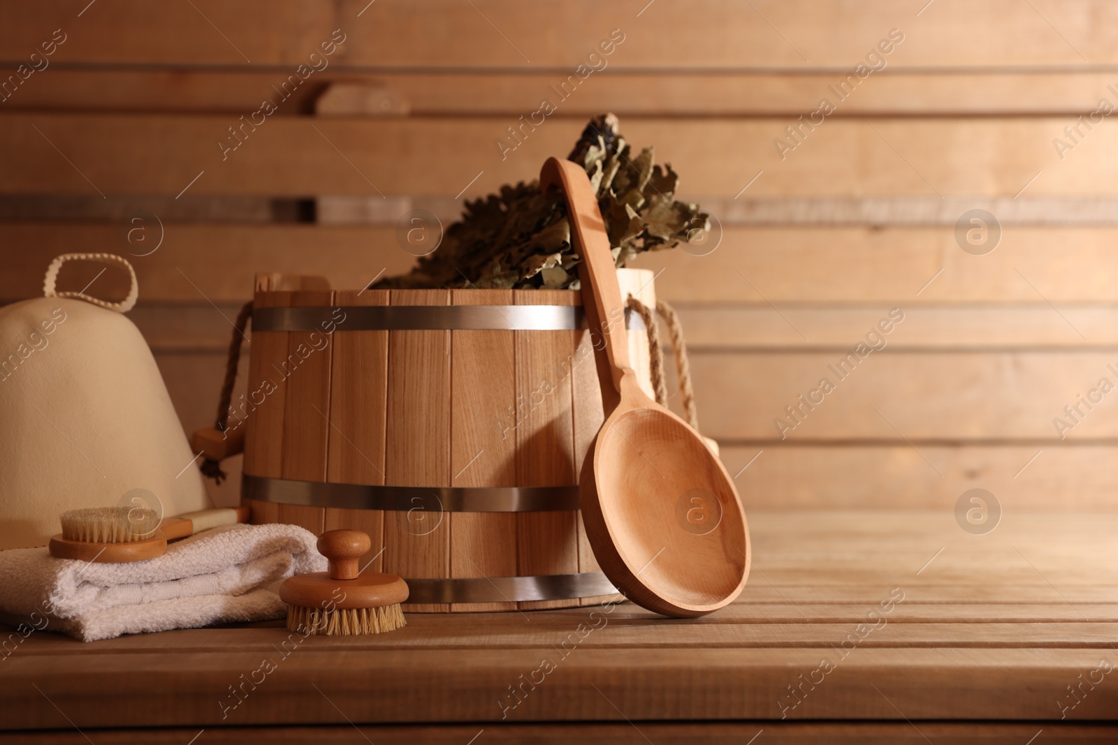 Photo of Bucket, whisk, massaging brushes and other equipment on wooden bench in sauna. Space for text