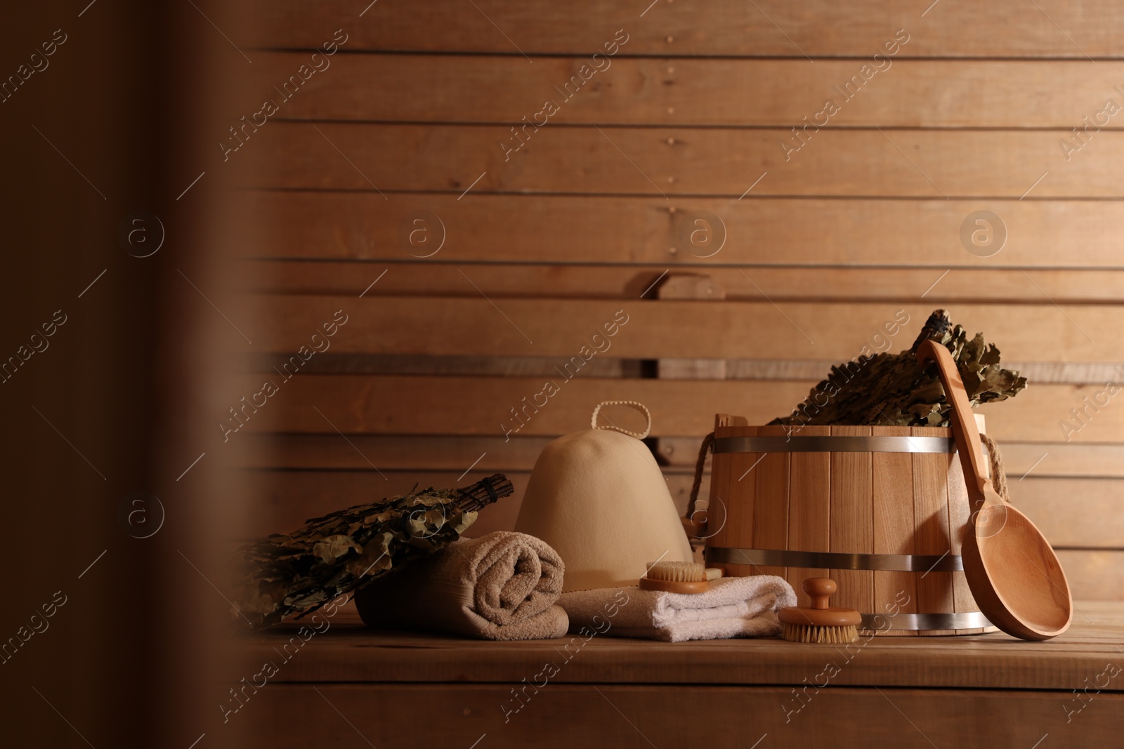 Photo of Bucket, whisk, massaging brushes and other equipment on wooden bench in sauna. Space for text