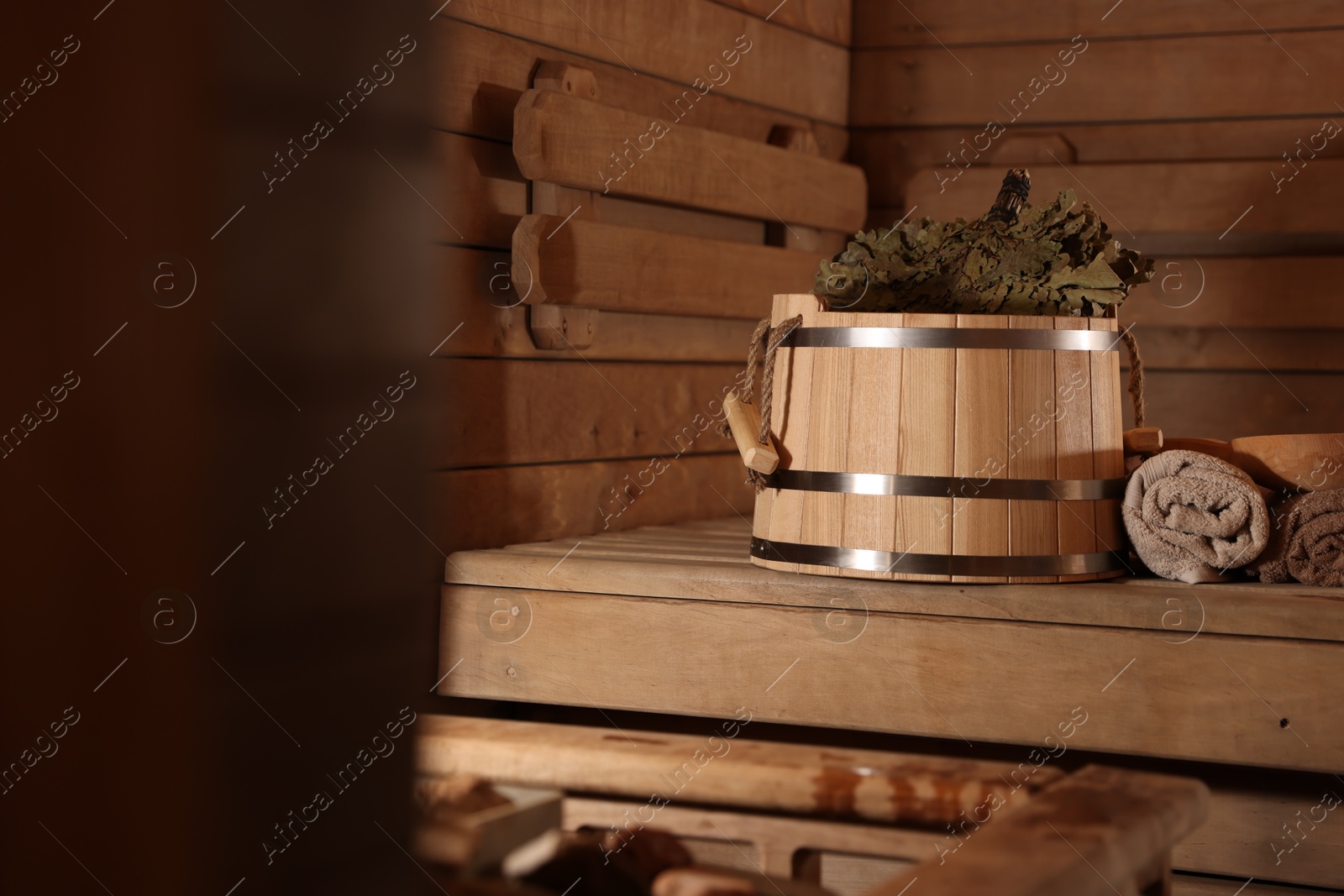 Photo of Bucket, whisk, ladle and towels on wooden bench in sauna