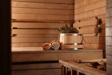 Photo of Bucket, whisk, ladle and towels on wooden bench in sauna