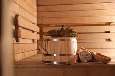 Photo of Bucket, whisk, ladle and towels on wooden bench in sauna