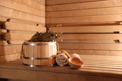 Photo of Bucket, whisk, ladle and towels on wooden bench in sauna. Space for text