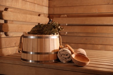 Photo of Bucket, whisk, ladle and towels on wooden bench in sauna