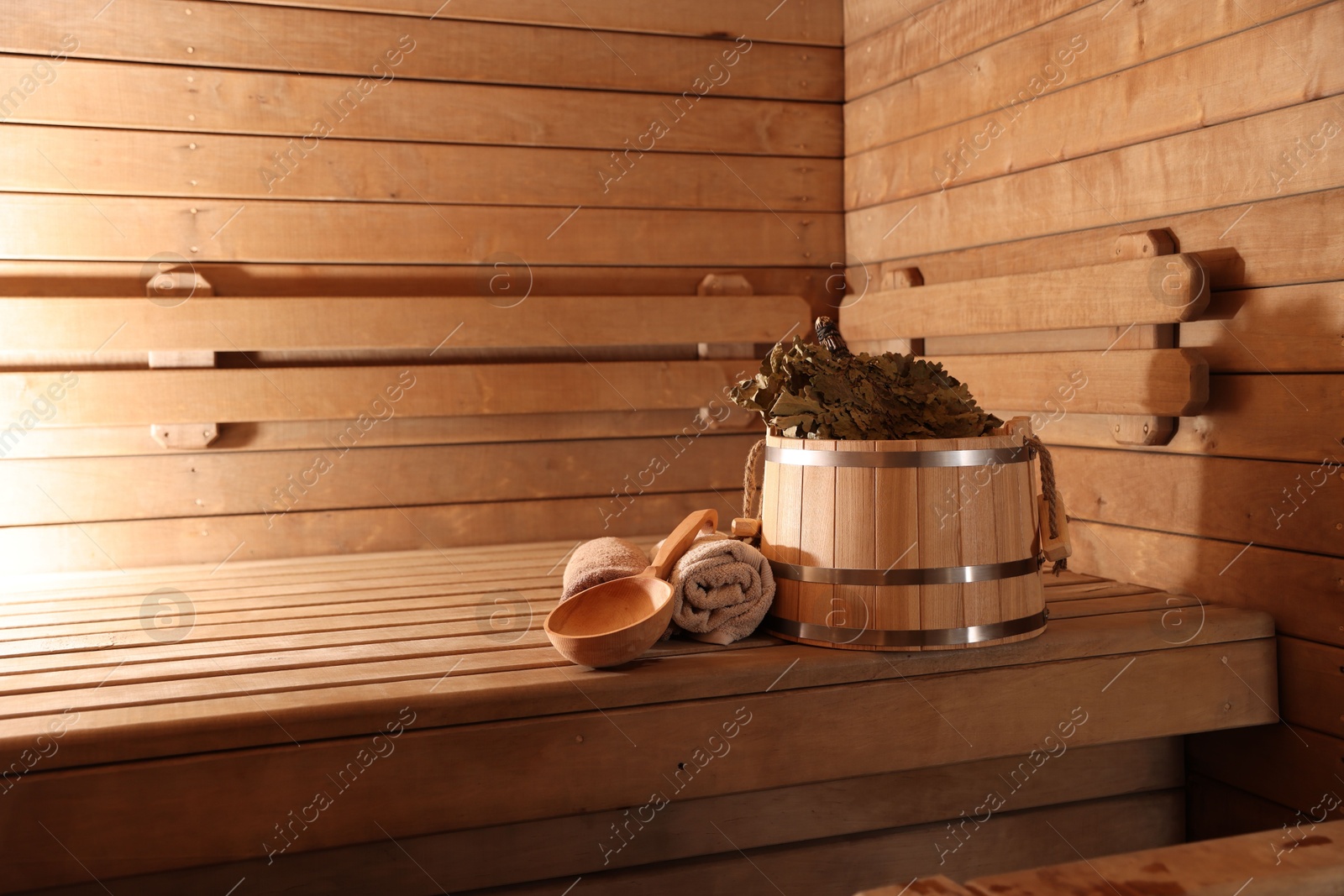 Photo of Bucket, whisk, ladle and towels on wooden bench in sauna. Space for text