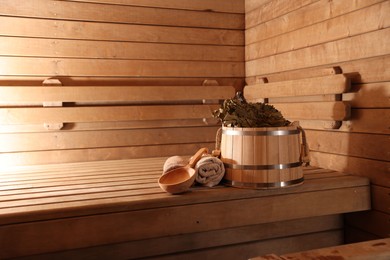 Photo of Bucket, whisk, ladle and towels on wooden bench in sauna. Space for text