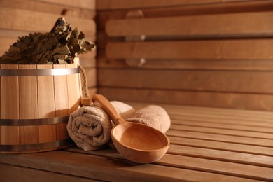 Photo of Bucket, whisk, ladle and towels on wooden bench in sauna. Space for text