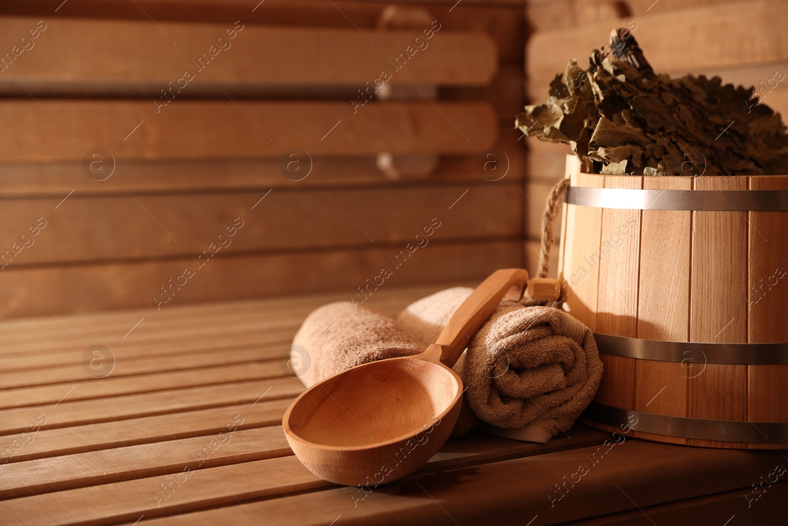 Photo of Bucket, whisk, ladle and towels on wooden bench in sauna. Space for text